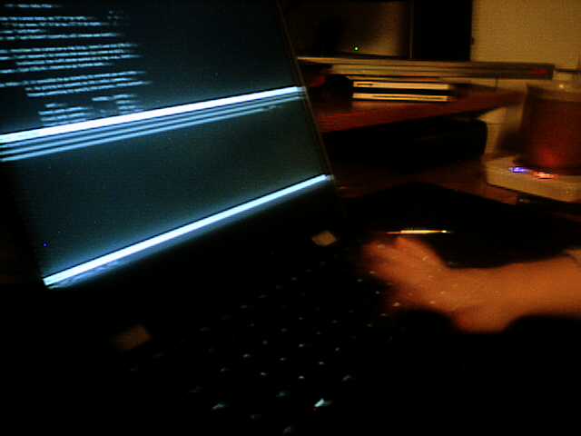 A dark shot of my laptop on my desk, my kid's hand motion-blurred over the keyboard