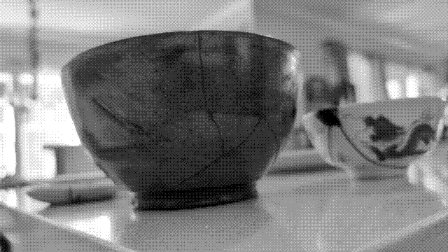 A grayscale photo of a large bowl with dark cracks tracing its surface. Behind it is a smaller bowl with a dragon motif, with a dark chip along the lip and two large cracks leading away from it.