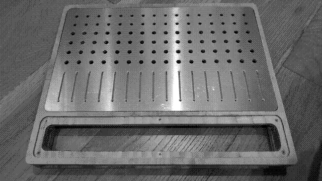 A front view of the mixer. The body is made of two pieces of plywood glued together, about one foot, one inch by one foot, four inches, by one inch and a half. In metric: 330 by 406 by 38 millimeters. There is a 235 by 386 millimeter aluminum faceplate inset about one centimeter from the edge of the wood body along its two short edges and one of its long ones, with sixteen columns of cutouts for controls. Two small holes at the top for toggle switches, four larger holes for potentiomenters, and a long slot for a sliding potentiometer. Just shy of one centimeter below this is a 65 by 386 millimeter cutout for a "miniplate," one centimeter from the edges of the wood with a one centimeter inner lip. Threaded inserts have been set in the middle of the long edges and in the corners. The body, plates, and cutouts all have their corners rounded by one centimeter.